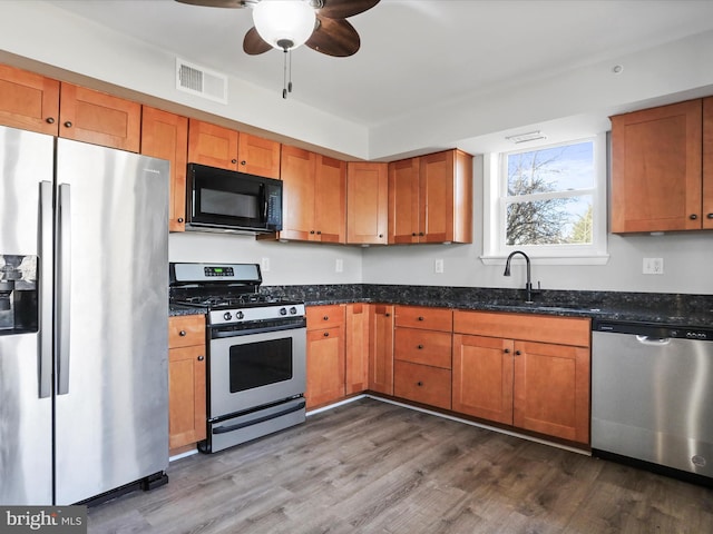 kitchen with hardwood / wood-style floors, stainless steel appliances, dark stone counters, and sink