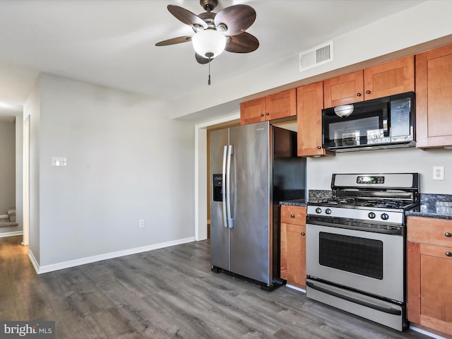 kitchen with dark wood-type flooring, appliances with stainless steel finishes, dark stone countertops, and ceiling fan