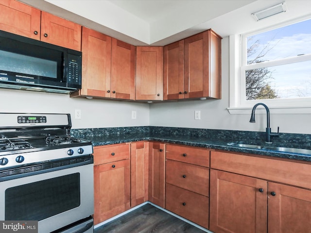 kitchen featuring stainless steel gas range oven, sink, dark stone counters, and dark hardwood / wood-style floors