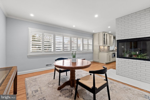 dining room featuring baseboards, light wood-type flooring, visible vents, and crown molding