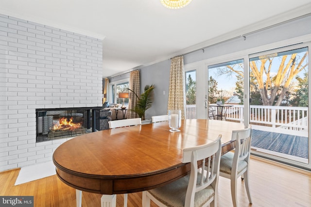 dining room with a brick fireplace, crown molding, and wood finished floors