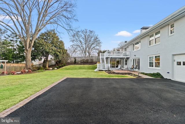 view of yard with a garage, a fenced backyard, stairs, a deck, and a patio area