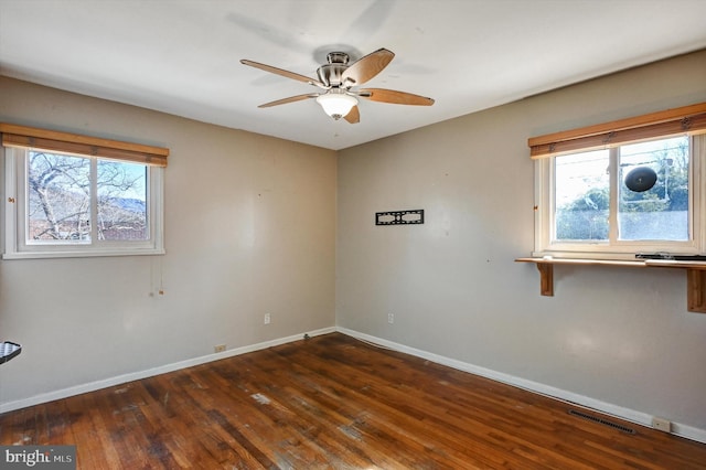 empty room with ceiling fan, a healthy amount of sunlight, and dark hardwood / wood-style floors