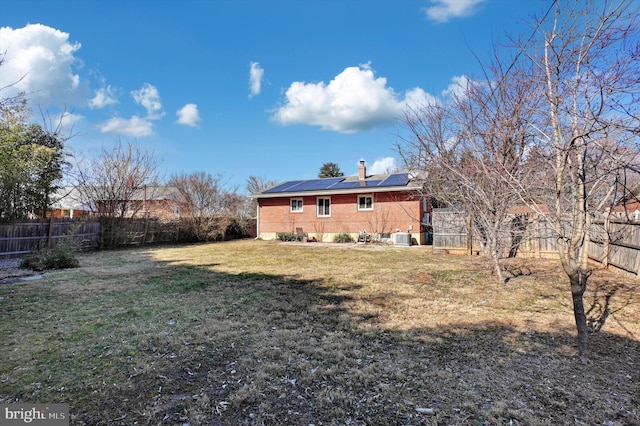 rear view of property featuring a yard, central AC, and solar panels