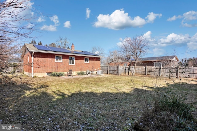 rear view of property featuring a lawn and solar panels