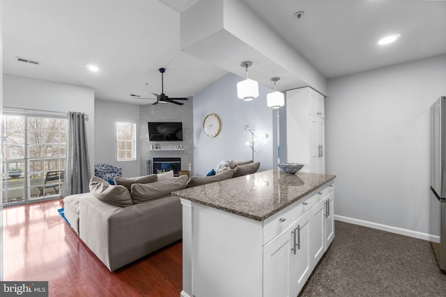 kitchen featuring dark stone countertops, visible vents, a fireplace, white cabinets, and open floor plan