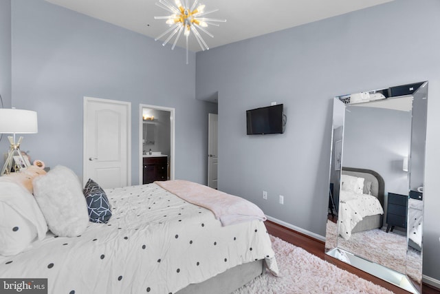 bedroom featuring baseboards, wood finished floors, ensuite bathroom, and ceiling fan with notable chandelier