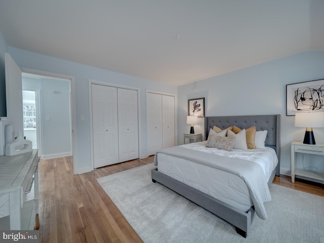 bedroom with lofted ceiling, light hardwood / wood-style floors, and multiple closets