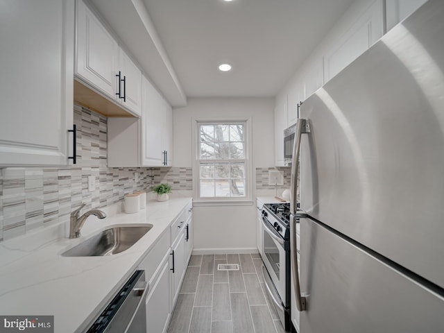 kitchen with sink, white cabinetry, appliances with stainless steel finishes, light stone countertops, and backsplash