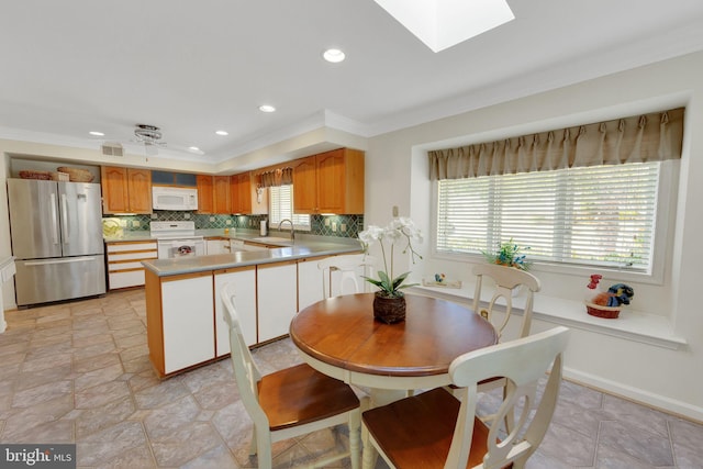 kitchen with crown molding, a skylight, kitchen peninsula, white appliances, and decorative backsplash