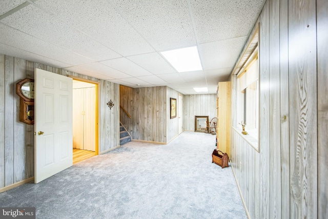 basement with carpet floors, a drop ceiling, and wood walls