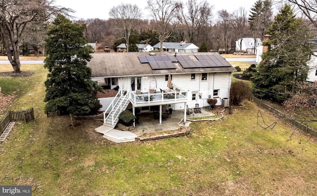 back of property with a wooden deck, a yard, a patio, and solar panels