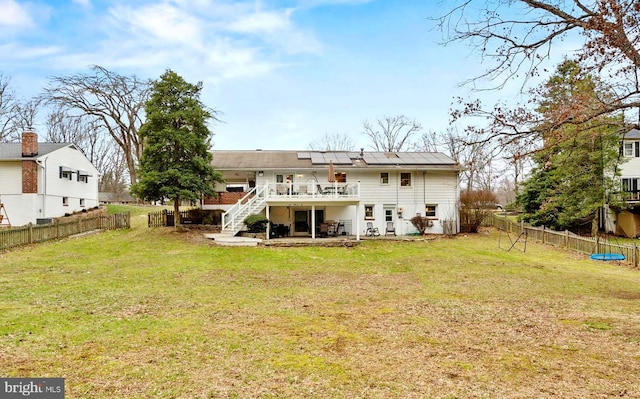 back of property with a yard, a deck, a patio area, and solar panels