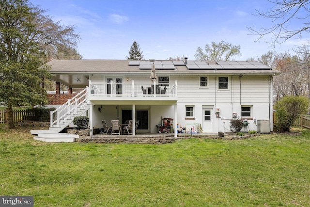 back of property with a patio area, a deck, solar panels, and a lawn