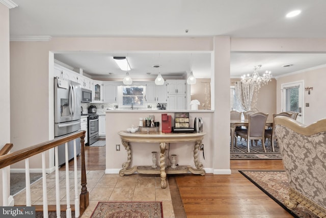 kitchen featuring sink, white cabinets, a chandelier, ornamental molding, and stainless steel appliances