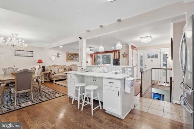 kitchen featuring a kitchen breakfast bar, light hardwood / wood-style floors, white cabinets, decorative light fixtures, and kitchen peninsula