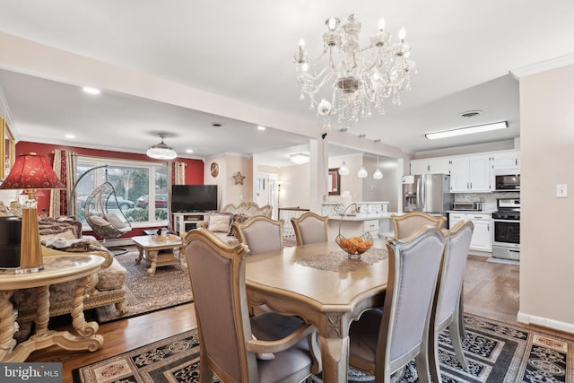 dining area with ornamental molding, sink, hardwood / wood-style floors, and a notable chandelier