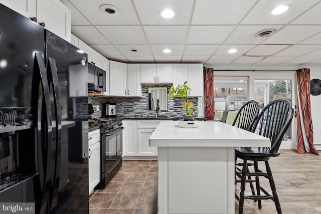 kitchen with white cabinetry, a center island, decorative backsplash, and black appliances