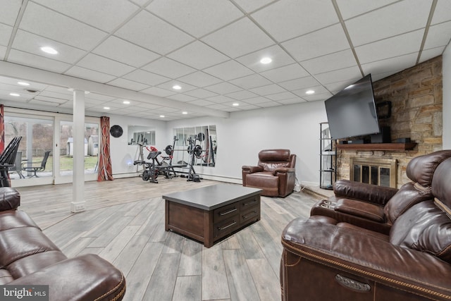 living room featuring ornate columns, a stone fireplace, baseboard heating, a drop ceiling, and light wood-type flooring