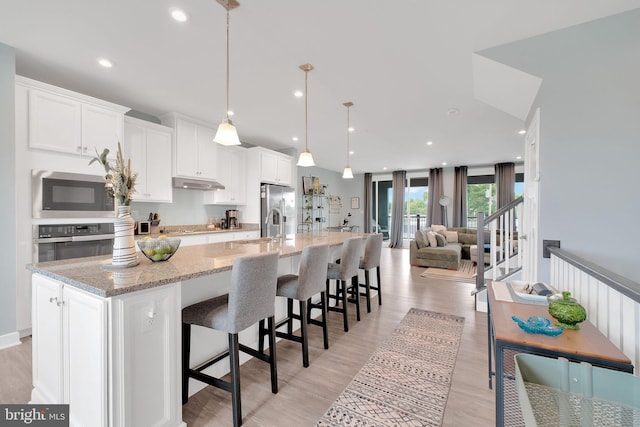 10056 American Pharoah Ln Unit 66, Laurel, MD 20723 - kitchen featuring stainless steel appliances, under cabinet range hood, a spacious island, white cabinets, and light wood-style floors