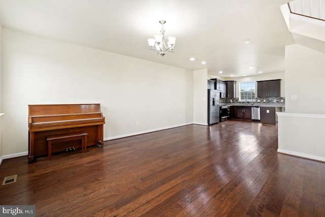 unfurnished living room with a chandelier, visible vents, dark wood finished floors, and baseboards