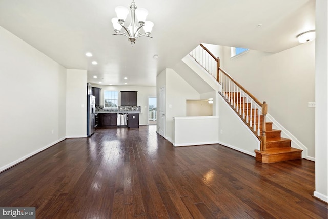 unfurnished living room featuring dark wood-type flooring, stairway, baseboards, and an inviting chandelier