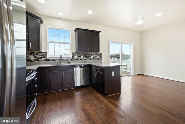 kitchen featuring a peninsula, a sink, a healthy amount of sunlight, appliances with stainless steel finishes, and light stone countertops