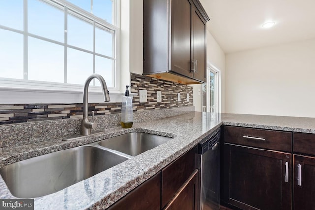 kitchen featuring dark brown cabinetry, dishwashing machine, light stone counters, a sink, and backsplash