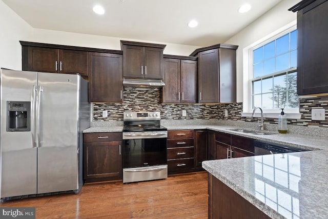 kitchen with dark wood-style flooring, light stone countertops, stainless steel appliances, under cabinet range hood, and a sink