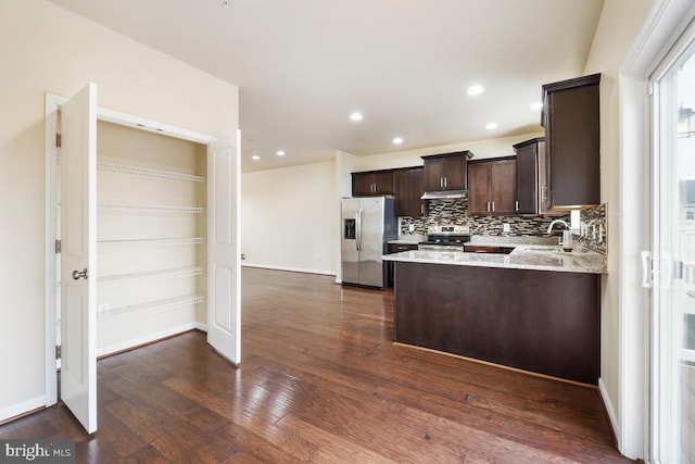 kitchen with dark wood finished floors, backsplash, appliances with stainless steel finishes, dark brown cabinets, and under cabinet range hood