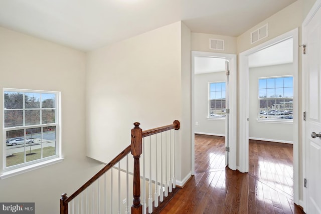 corridor with dark wood-style floors, baseboards, visible vents, and an upstairs landing