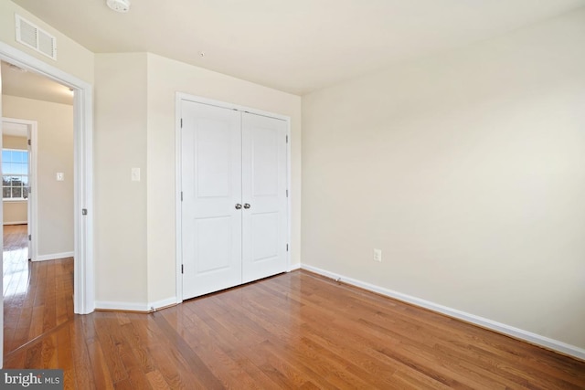 unfurnished bedroom featuring baseboards, a closet, visible vents, and wood finished floors