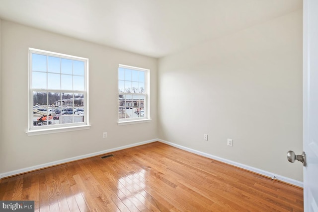 spare room with light wood finished floors, visible vents, and baseboards