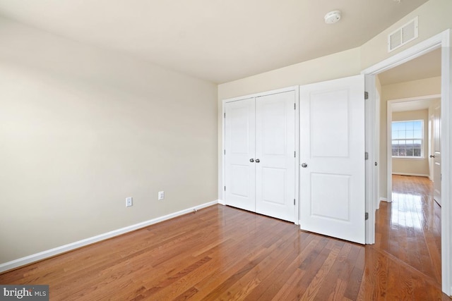 unfurnished bedroom with dark wood-type flooring, a closet, visible vents, and baseboards