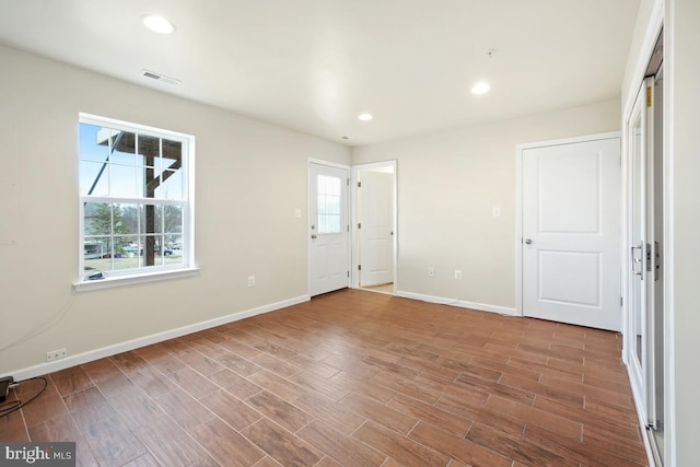 empty room with a wealth of natural light, visible vents, baseboards, and wood finished floors