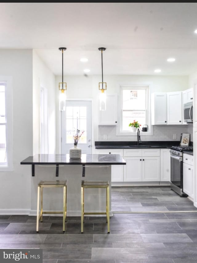 kitchen with wood finish floors, a sink, white cabinets, appliances with stainless steel finishes, and dark countertops