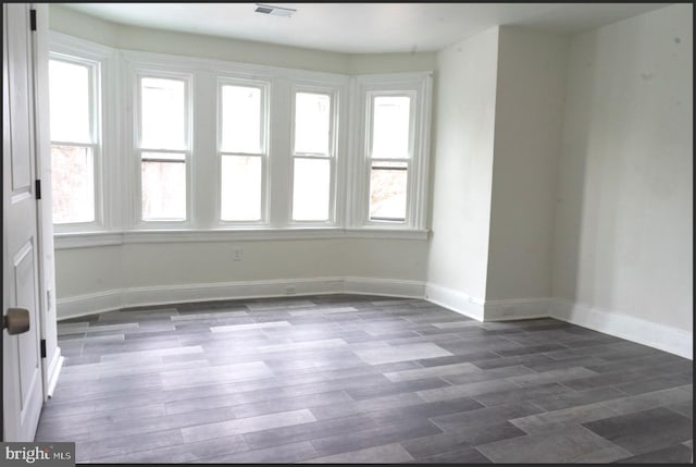 empty room featuring a wealth of natural light, baseboards, and dark wood-type flooring