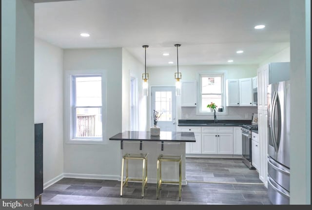 kitchen with a sink, dark countertops, appliances with stainless steel finishes, white cabinets, and wood tiled floor