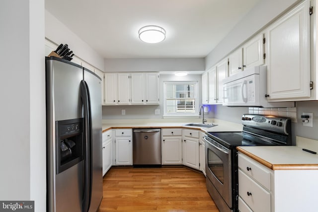 kitchen with light wood-style floors, appliances with stainless steel finishes, a sink, and white cabinets