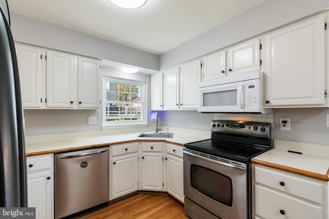 kitchen with a sink, light wood finished floors, white cabinetry, and stainless steel appliances