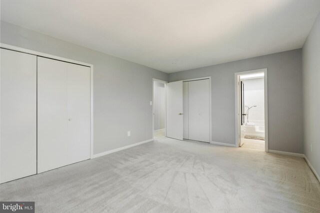 unfurnished bedroom with light carpet, baseboards, multiple closets, and connected bathroom