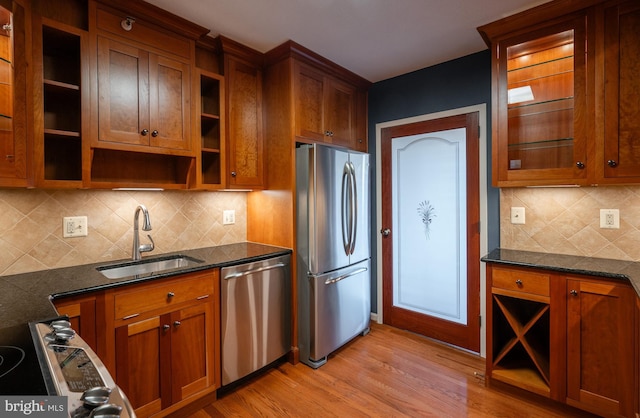 kitchen featuring stainless steel appliances, sink, dark stone counters, and light hardwood / wood-style flooring