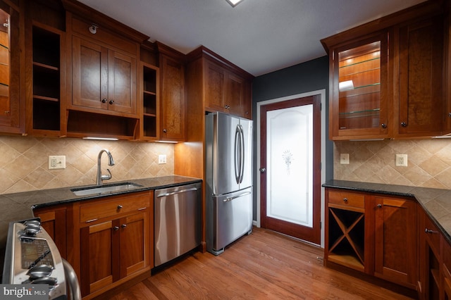 kitchen with sink, appliances with stainless steel finishes, backsplash, light hardwood / wood-style floors, and dark stone counters