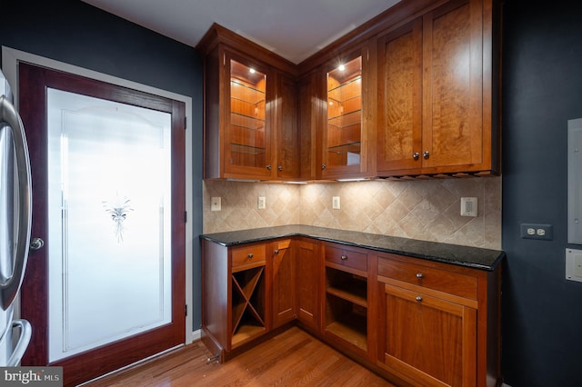 kitchen featuring dark stone countertops, decorative backsplash, light hardwood / wood-style flooring, and stainless steel refrigerator