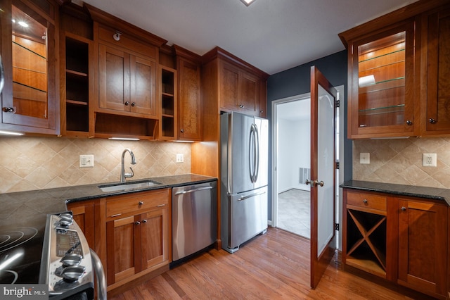 kitchen with stainless steel appliances, sink, light hardwood / wood-style floors, and dark stone counters