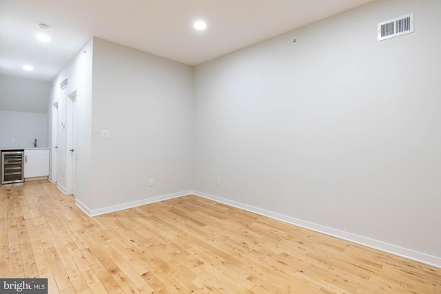 spare room featuring bar area, wine cooler, and light hardwood / wood-style flooring