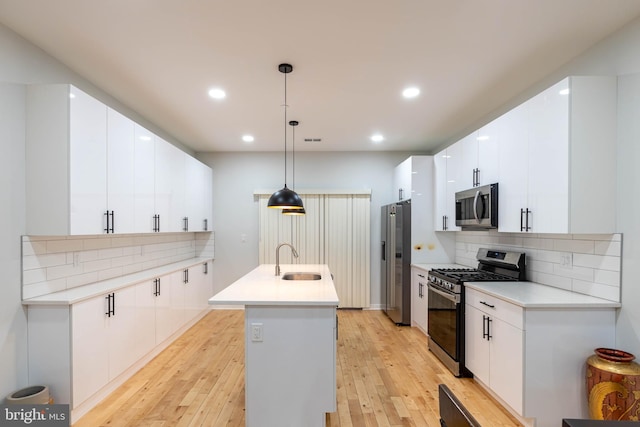 kitchen featuring appliances with stainless steel finishes, decorative light fixtures, white cabinetry, sink, and a center island with sink