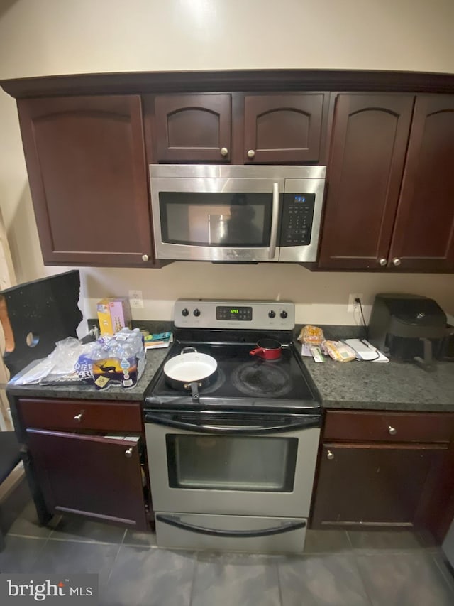 kitchen featuring dark brown cabinetry, stainless steel appliances, and dark tile patterned flooring