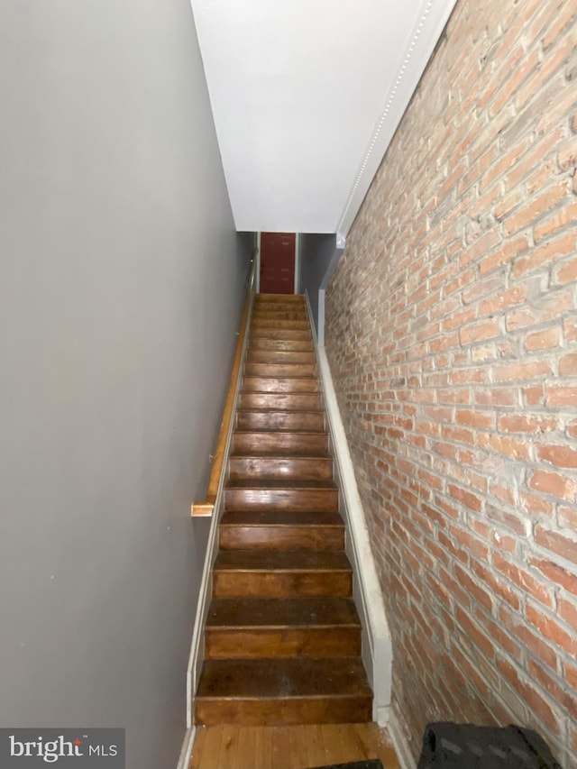 staircase featuring brick wall and wood-type flooring