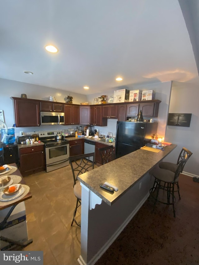 kitchen with appliances with stainless steel finishes, a kitchen bar, kitchen peninsula, and sink